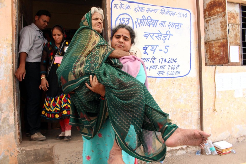 Een oudere vrouw wordt uit het stembureau geholpen.