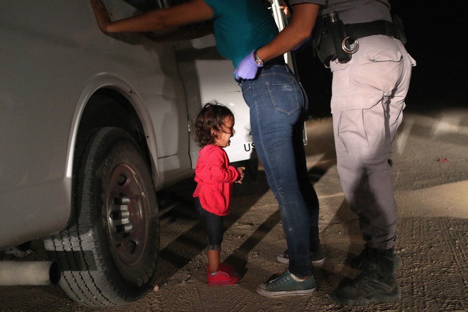 Een kind is overstuur terwijl de moeder gefouilleerd wordt aan de Amerikaans-Mexicaanse grens. 