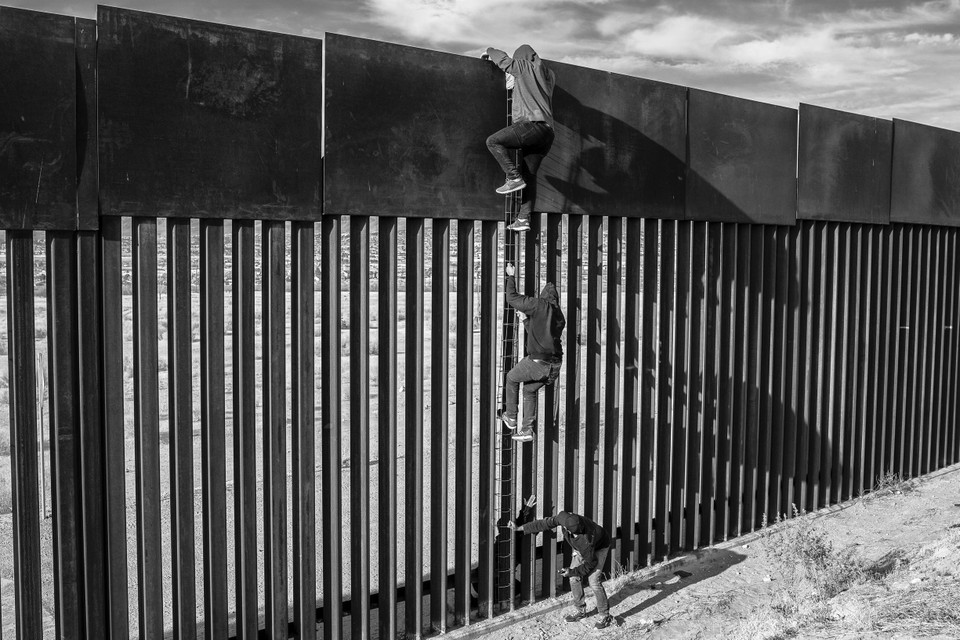 Migranten proberen de grensmuur tussen Mexico en de Verenigde Staten over te klimmen.