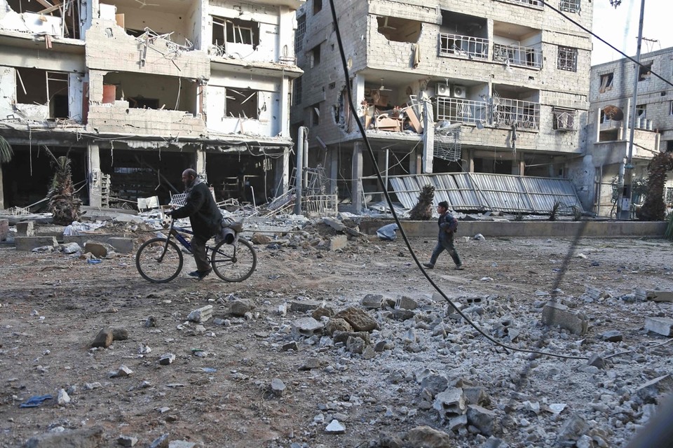 Inwoners fietsen en wandelen langs een straat die de dag ervoor getroffen werd door bombardementen. 