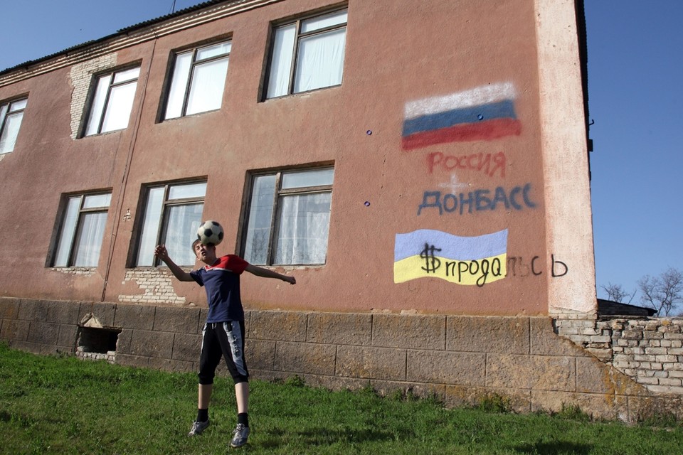 Een jongetje speelt met een bal, achter hem staan op de muur de vlaggen van Rusland en Oekraïne. 